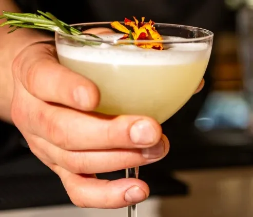 A signature cocktail served up, garnished with rosemary and marigold